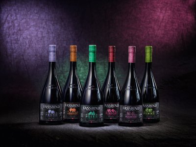 Sechs Flaschen mit bunten Kappen stehen auf einem dunklen Hintergrund, jede Flasche hat ein einzigartiges Etikett und Design.