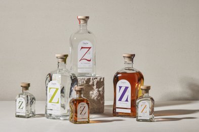 Eine stilvolle Anordnung von Obstbrandflaschen, darunter klare und bernsteinfarbene Flüssigkeiten, auf einem Natursteinblock.