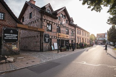 Ein historisches Gebäude mit Backsteinfassade und Holzverzierungen, das eine Destillerie beherbergt, ist im Vordergrund sichtbar.