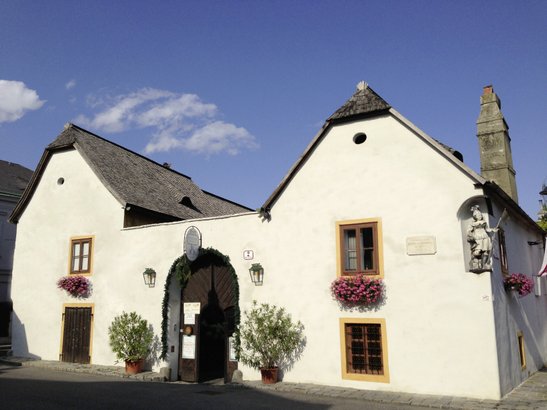 Ein charmantes, weißes Gebäude mit einem geschwungenen Dach und bunten Blumen an den Fenstern, unter einem blauen Himmel.