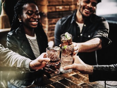 Eine Gruppe von Freunden hebt ihre Gläser an, während sie in einer gemütlichen Bar zusammen lachen und feiern.