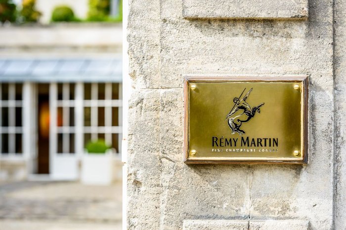 Ein goldener Schild mit dem Logo von Rémy Martin, der an einer steinernen Wand befestigt ist, vor einem unscharfen Hintergrund.