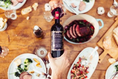 Der Tisch ist reich gedeckt mit Speisen, während eine Hand eine Flasche Rotwein präsentiert, die im Fokus steht.
