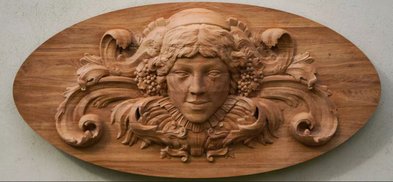 Eine kunstvoll geschnitzte Holzplatte zeigt ein Gesicht mit sanften Zügen und floralen Verzierungen, die Eleganz ausstrahlen.