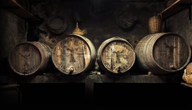 Dunkle, rustikale Umgebung mit vier alten Holzfässern, die mit dem Logo der Glendalough Distillery versehen sind.