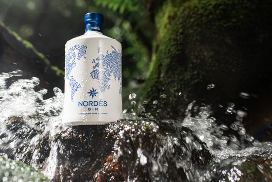 Eine Flasche Nordés Gin steht auf einem moosbedeckten Stein, umgeben von sprudelndem Wasser in einer natürlichen Umgebung.
