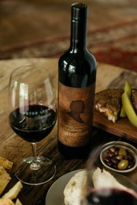 Ein stilvolles Arrangement aus einem Rotwein, einem Glas und herzhaften Snacks wie Sandwiches und Oliven auf einem Holzbrett.