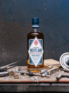 Eine Flasche Westland Whiskey steht auf einem Holzwerkbank, umgeben von Werkzeugen und Metallspänen.