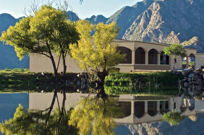 Ein modernes Gebäude steht am Ufer eines Sees, umgeben von leuchtend gelben Bäumen und reflektiert in der ruhigen Wasseroberfläche.