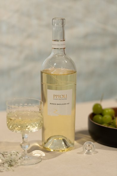 Eine Flasche Weißwein steht neben einem eleganten Glas auf einem Tisch, umgeben von frischen Trauben und zarten Blumen.