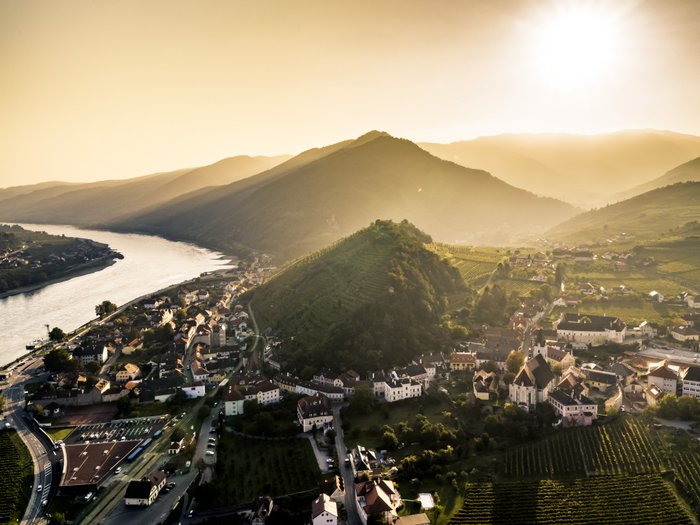 Ein atemberaubender Blick auf ein Dorf, umgeben von Weinbergen und Bergen, mit einem glitzernden Fluss im Vordergrund.
