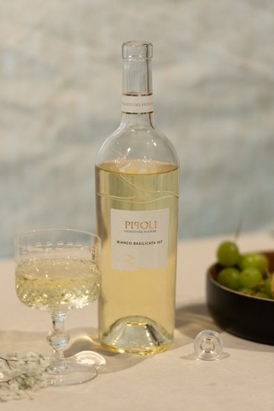 Eine Flasche Weißwein steht neben einem eleganten Glas auf einem Tisch, umgeben von frischen Trauben und zarten Blumen.