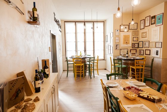 Ein einladendes Restaurant mit hellen Wänden, bunten Stühlen und einem Tisch, der mit Käse und Wurstplatten gedeckt ist.