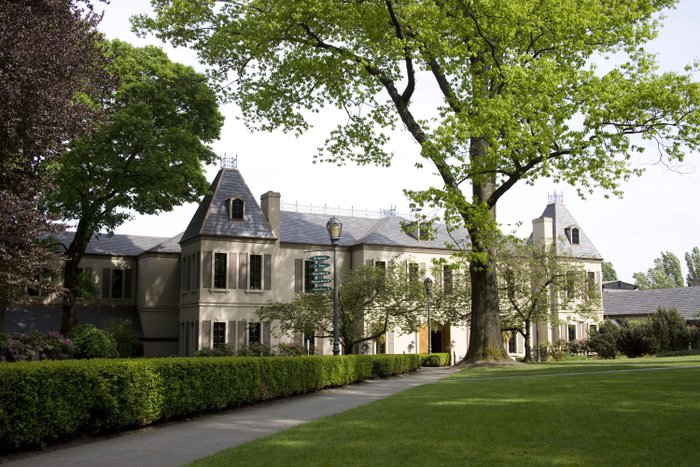 Ein charmantes Gebäude mit einem spitzen Dach und dekorativen Fenstern, eingebettet in eine grüne Landschaft mit blühenden Pflanzen.