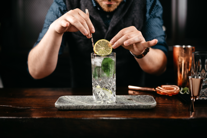 Ein Barkeeper dekoriert einen Cocktail mit einer Limettenscheibe und frischen Minzblättern in einem eleganten Glas.