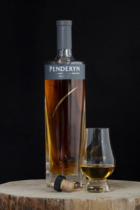 Eine elegante Flasche Penderyn Whisky steht neben einem Glas, das mit goldenem Whisky gefüllt ist, auf einem rustikalen Holzuntergrund.