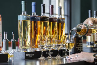 Die Szene zeigt eine Hand, die Whisky in ein Glas gießt, während die Penderyn-Flaschen im Hintergrund leuchten.