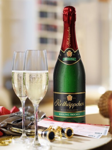 Eine Flasche Rotkäppchen Riesling Sekt steht neben zwei Gläsern mit sprudelndem Sekt auf einem eleganten Tisch.