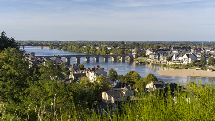 Eine malerische Aussicht auf einen Fluss, der durch eine grüne Landschaft fließt, mit einem beeindruckenden Steinbogenbrücke im Hintergrund.