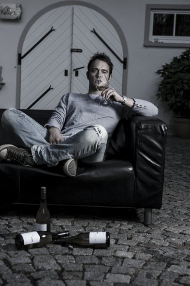 Ein Mann sitzt entspannt auf einem schwarzen Sofa, während er ein Glas Wein genießt und nachdenklich in die Ferne blickt.