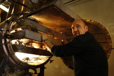 Der Mann mit einem ernsten Gesichtsausdruck hebt eine Metallplatte an, um Kräuter in eine leuchtende Kammer zu legen, die für die Herstellung verwendet wird.