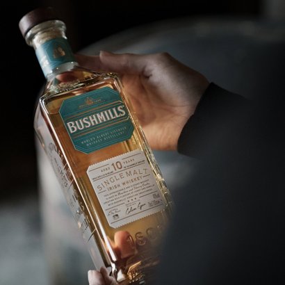 Eine Hand hält eine Flasche Bushmills 10 Jahre alten Single Malt Irish Whiskey, die in sanftem Licht glänzt.