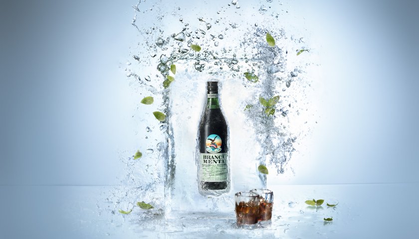 Die Flasche Branca Menta wird von Wasser und Minzblättern umgeben, was eine erfrischende Atmosphäre schafft.