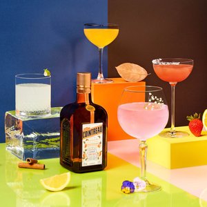 Ein stilvolles Arrangement von Cocktails in verschiedenen Farben, umgeben von frischen Früchten und einer Flasche Cointreau.