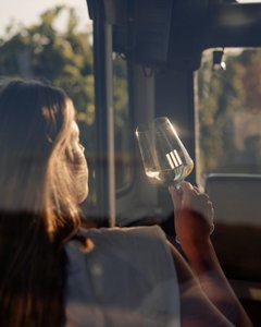 Die Silhouette einer Frau mit langen Haaren ist zu sehen, während sie ein Glas in der Hand hält und das Licht bewundert.