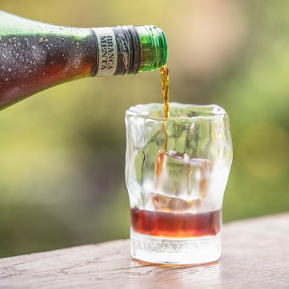 Ein erfrischendes Getränk wird in ein Glas gegossen, während die Flasche mit Wassertröpfchen bedeckt ist und im Hintergrund verschwommen ist.