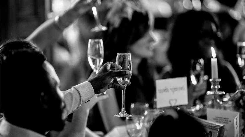 Eine Gruppe von Menschen hebt Gläser in einem festlichen Ambiente, während eine Kerze auf dem Tisch flackert.