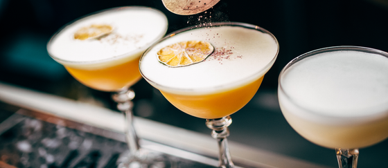 Ein Barkeeper streut mit einem Sieb Gewürze auf einen Cocktail mit einer Scheibe getrockneter Zitrone als Garnitur.