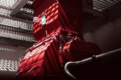In einem industriellen Raum dominiert eine rote Maschine, deren Details durch die einfallenden Lichtstrahlen hervorgehoben werden.
