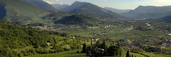 Eine atemberaubende Aussicht auf Weinberge und ein malerisches Dorf, eingebettet in eine grüne Hügellandschaft mit Bergen im Hintergrund.