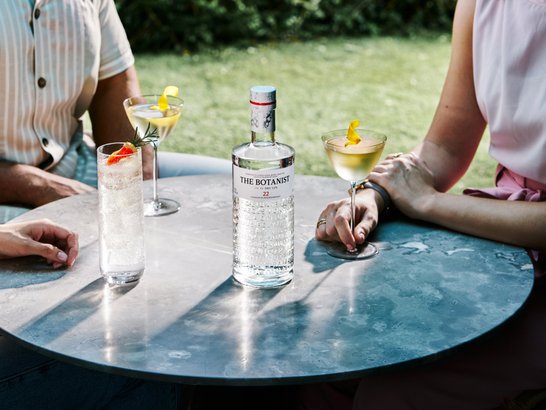 Die Sonne scheint auf einen Tisch mit Cocktails, während zwei Freunde in lässiger Kleidung eine gesellige Zeit verbringen.