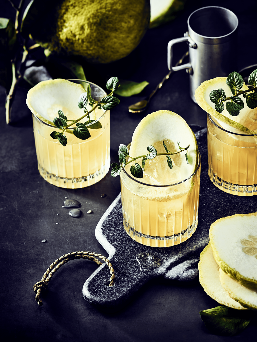 Drei Gläser mit eisgekühltem Getränk, dekoriert mit frischen Minzblättern, stehen auf einem eleganten, dunklen Tisch.