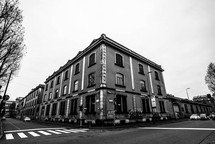 Ein ehemaliges Industriegebäude mit einer auffälligen Beschriftung an der Seite, umgeben von einer leeren Straße und Bäumen.