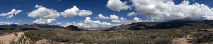 Eine weite Landschaft mit sanften Hügeln und Bergen unter einem strahlend blauen Himmel mit großen, weißen Wolken.